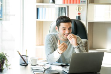 Genç bir işadamı evde oturuyor ve cep telefonu ve bilgisayar ile bir masanın üzerinde çalışıyor ve başvuru yoluyla buluşuyor..