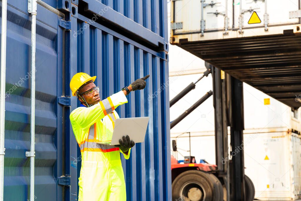 Import and Export concept. Foreman using laptop computer in the port of loading goods. Businessman with safety equipment working at warehouse.