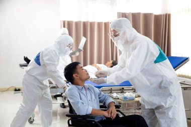 Koruyucu giysili bir doktor hastane muayene odasında bir hastanın virüsünü test ediyor..