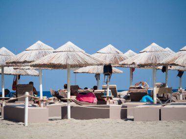 Beyaz hasır şemsiyeler altında yumuşak şezlong sahilde dinlenin.