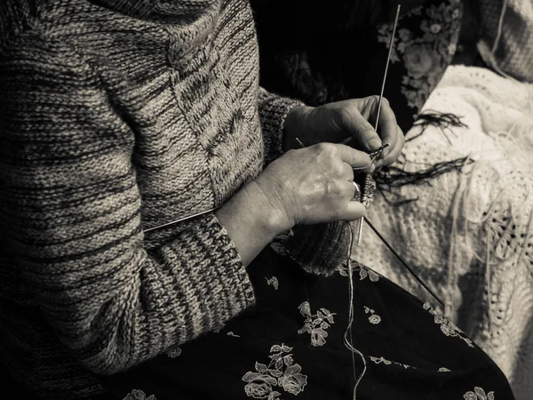 Detail of an old lady knitting a wool blanket.