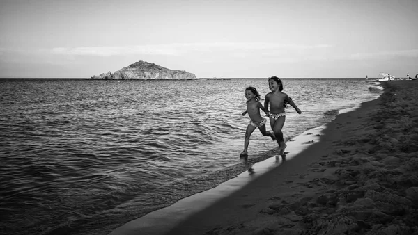 Little sisters run happy on the sand along the seashore at sunse