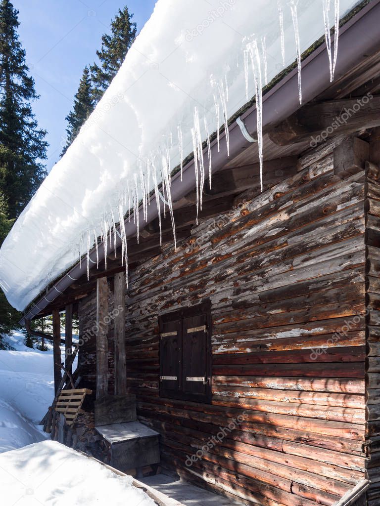 Ice stalactites hanging from the roof of a wooden house in the m