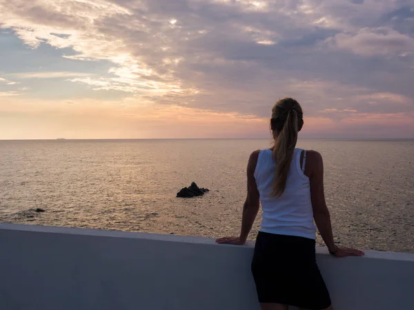 Blonde woman watching the sunset from a terrace overlooking the