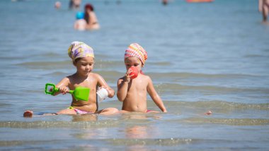 Two little girls with bandana playing in the sea. clipart