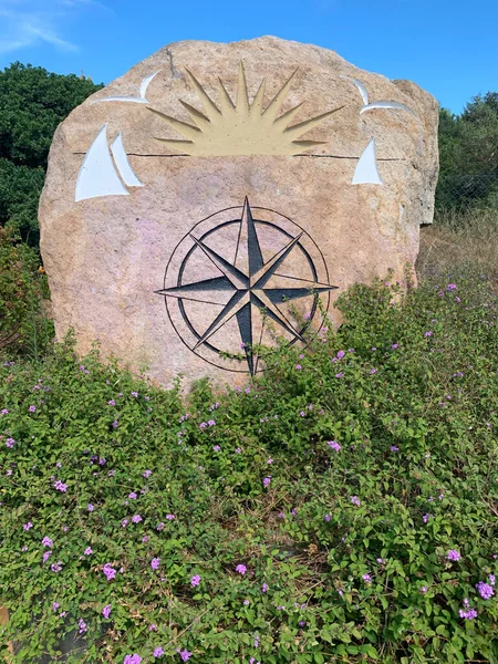 Compass rose painted on a rock surrounded by green bushes.