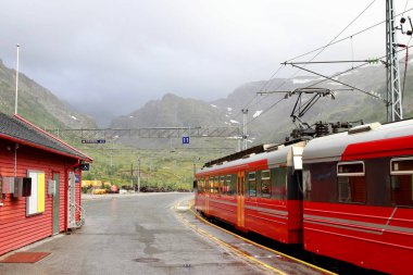 View of Voss mountain train stopped at Myrdal train station with snowy peaks on backgound, Norway. clipart