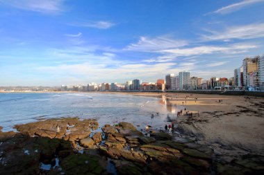 Güneşli bir Paskalya gecesi sırasında arka planda Gijon şehir merkezi ile San Lorenzo plajının ana görünümü, Asturias, Ispanya.