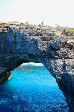 Bali Denizi 'ni Endonezya' nın Nusa Penida adasının en harika yerlerinden biri olan Kırık Sahile bağlayan kaya kemerinin tepesindeki genç anne..