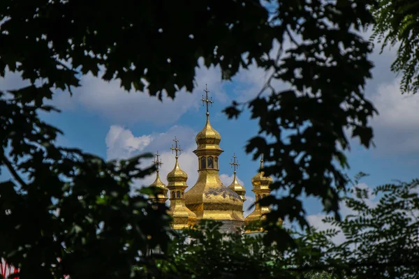 Ağaçlar arasında mavi gökyüzüne karşı altın kubbeleri olan Ortodoks Kilisesi