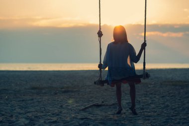 Yalnız ve güzel bir kadın sahilde sallanıyor. Tahta bir köprüde gün batımında yalnız bir kadın. Yalnızlar. biçimli soyut Ton