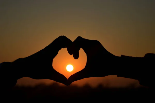 Couple making love shape with the sun on the frame