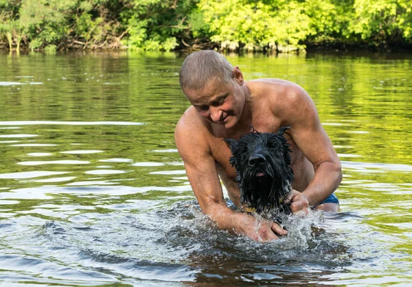 Love of animals and kindness. A man is playing with his dog on the river bank