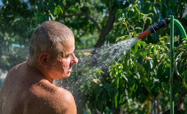 Man is washing under the spray of a summer shower