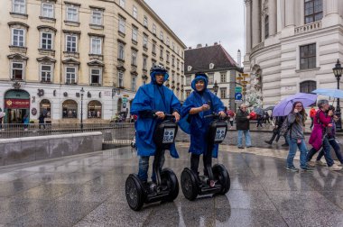 Vienna, Austria - July 13, 2019: Two tourists in raincoats looking at tourist architectural sights on the streets of Vienna, Austria. Autumn weather in Vienna. Segway as a city vehicle