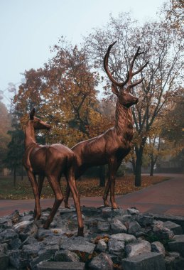 Misty autumn park and bronze deer statues