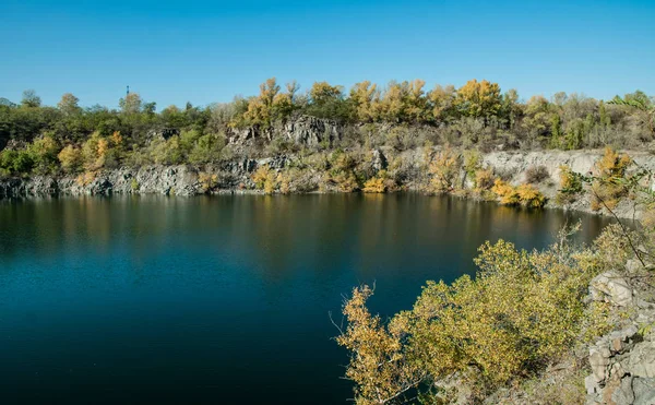 Autumn countryside landscape in New England, USA. Old abandoned quarry, deep lake and trees with yellow autumn foliage. Sunny picturesque autumn day