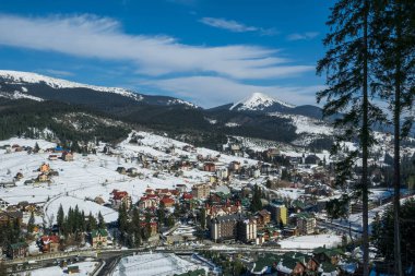 Bukovel, İvano-Frankivsk / Ukrayna - Mart 03 2019: Ukrayna 'nın Karpat Dağları' ndaki Bukovel tatil beldesinde bir dağ yamacında karlı kayak yamacı. Modern kayak asansörü ve ahşap turist kulübeleri