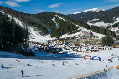 Bukovel, İvano-Frankivsk / Ukrayna - Mart 03 2019: Ukrayna 'nın Karpat Dağları' ndaki Bukovel tatil beldesinde bir dağ yamacında karlı kayak yamacı. Modern kayak asansörü ve ahşap turist kulübeleri
