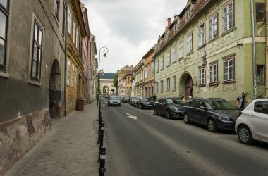 Brasov, Transilvanya, Romanya - 09 Haziran 2018: Romanya 'nın Transilvanya kentindeki eski Brasov kentinin dar ortaçağ caddesinde arabalar. Antik binalar ve otoyolda ulaşım. Doğu Avrupa 'da şehir hayatı