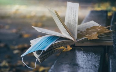 Sonbahar bahçesinin arka planında açık bir kitap ve tıbbi maske. Karantina ve kendini izole etme