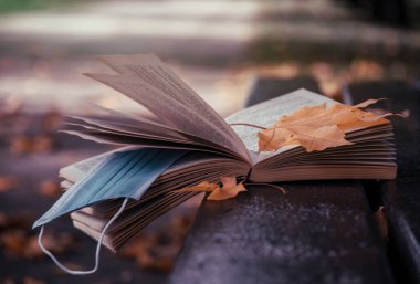 Sonbahar bahçesinin arka planında açık bir kitap ve tıbbi maske. Karantina ve kendini izole etme