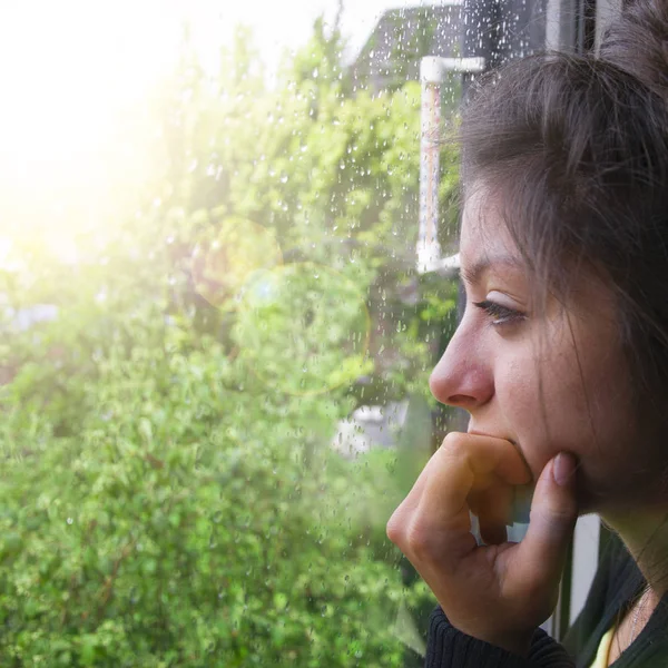 Sad girl looks out the window its raining. Woman with nice looking hear — Stock Photo, Image