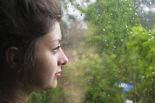 Sad girl looks out the window its raining. Woman with nice looking hear