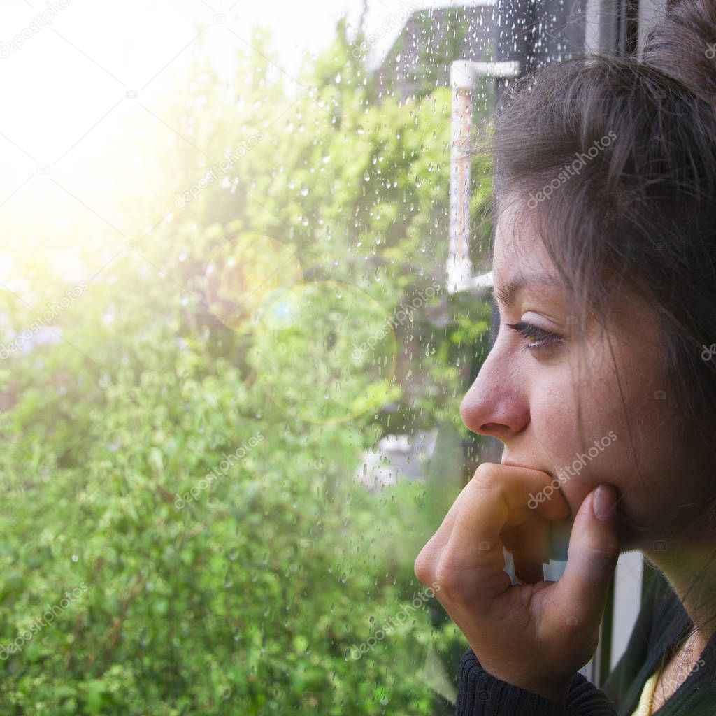 Sad girl looks out the window its raining. Woman with nice looking hear