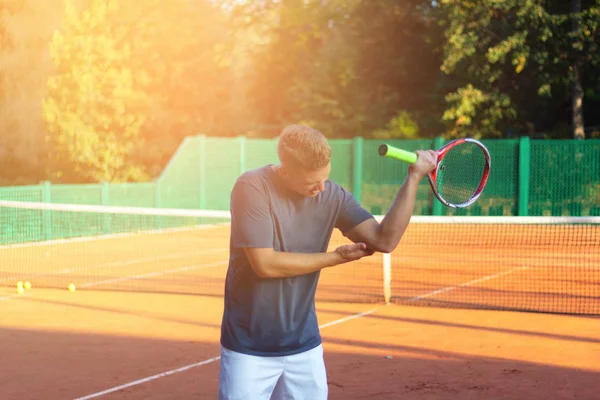 Un bell'uomo sul campo da tennis. Giovane tennista. Dolore al gomito con luce solare sullo sfondo — Foto Stock