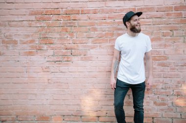 Sakallı, beyaz, boş tişörtlü, beysbol şapkalı, logonuz için yeri olan yakışıklı bir hippi mankeni.