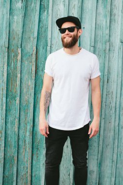 Sakallı, beyaz, boş tişörtlü, beysbol şapkalı, logonuz için yeri olan yakışıklı bir hippi mankeni.