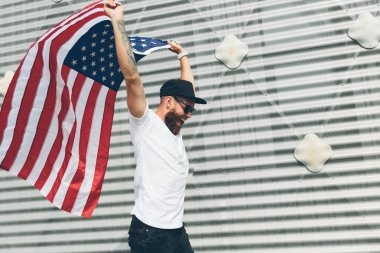 Mutlu hipster adam Amerikan veya ABD bayrağı tutarak. O rahat kıyafetler giyiyor.
