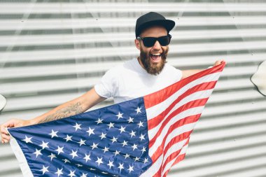 Mutlu hipster adam Amerikan veya ABD bayrağı tutarak. O rahat kıyafetler giyiyor.