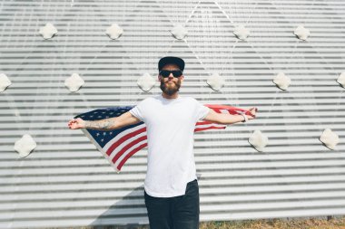 Mutlu hipster adam Amerikan veya ABD bayrağı tutarak. O rahat kıyafetler giyiyor.