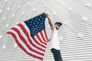Mutlu hipster adam Amerikan veya ABD bayrağı tutarak. O rahat kıyafetler giyiyor.