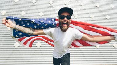 Mutlu hipster adam Amerikan veya ABD bayrağı tutarak. O rahat kıyafetler giyiyor.