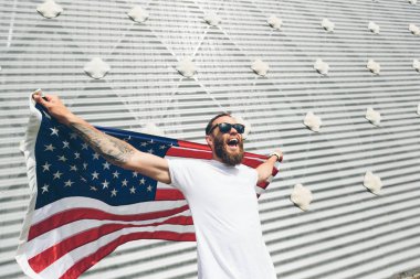 Mutlu hipster adam Amerikan veya ABD bayrağı tutarak. O rahat kıyafetler giyiyor.