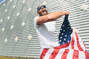 Mutlu hipster adam Amerikan veya ABD bayrağı tutarak. O rahat kıyafetler giyiyor.