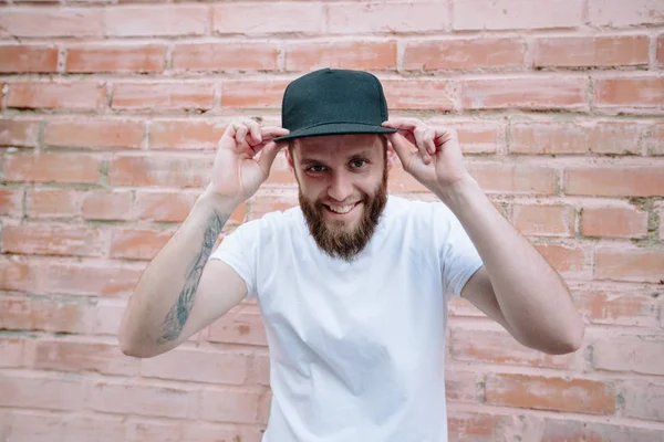 Hipster handsome male model with beard wearing white blank t-shirt and a baseball cap with space for your logo or design in casual urban style