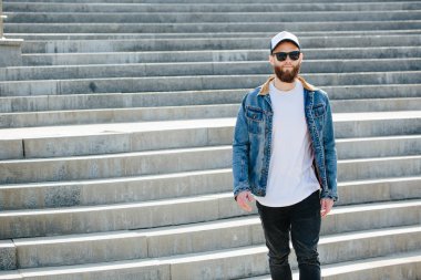 Siyah kot pantolon, tişört ve bir beyzbol şapkası giyen yürüyen hipster adam