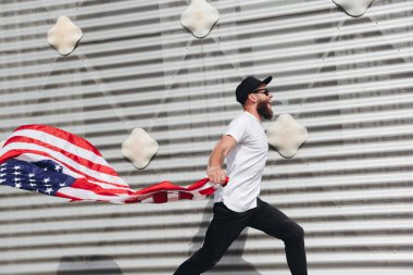 Mutlu hipster adam Amerikan veya ABD bayrağı tutarak. O rahat kıyafetler giyiyor.