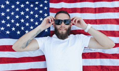 Mutlu hipster adam Amerikan veya ABD bayrağı tutarak. O rahat kıyafetler giyiyor.