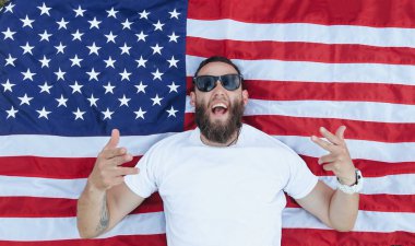Mutlu hipster adam Amerikan veya ABD bayrağı tutarak. O rahat kıyafetler giyiyor.
