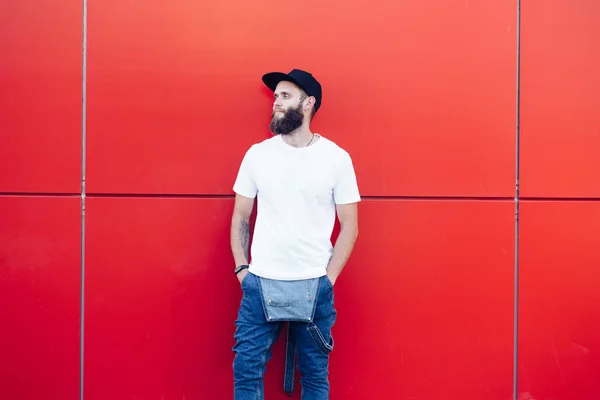 Hipster handsome male model with beard wearing white blank t-shirt and a baseball cap with space for your logo