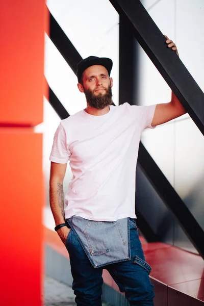 Hipster handsome male model with beard wearing white blank t-shirt and a baseball cap with space for your logo