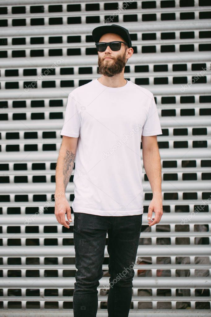 Hipster handsome male model with beard wearing white blank t-shirt and a baseball cap with space for your logo