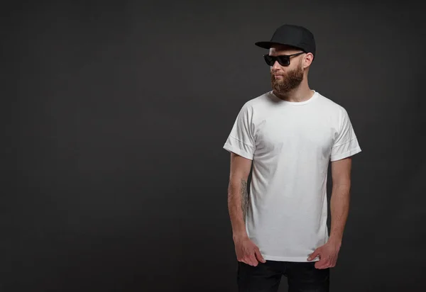 Hipster handsome male model with beard wearing white blank t-shirt and a baseball cap with space for your logo or design in casual urban style — Stock Photo, Image