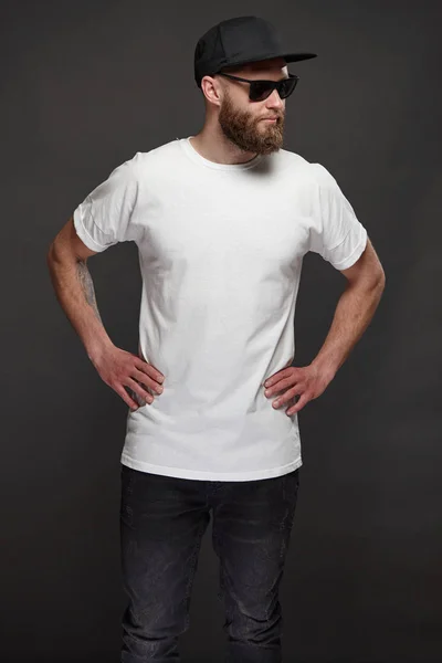 Hipster handsome male model with beard wearing white blank t-shirt and a baseball cap with space for your logo or design in casual urban style — Stock Photo, Image