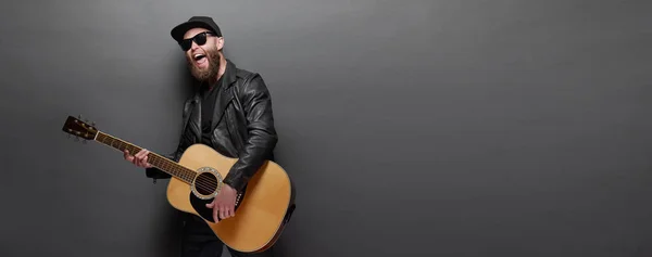 Guitarrista cantando en estudio de música. Guitarrista Hipster con barba y ropa negra tocando la guitarra acústica —  Fotos de Stock